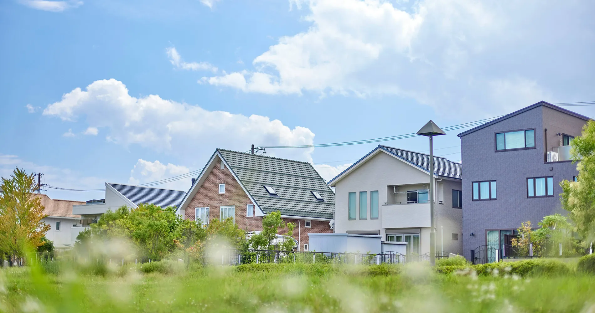 介護施設周辺の住宅地と緑地。青空の下、複数の建物が見える外構環境